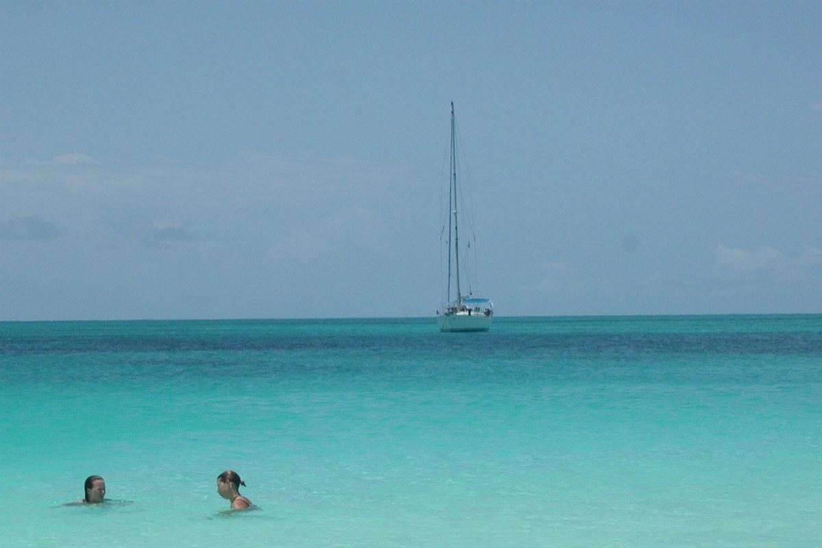 Segelyacht vor Anker über türkisem Wasser, im Vordergrund zwei Schwimmer