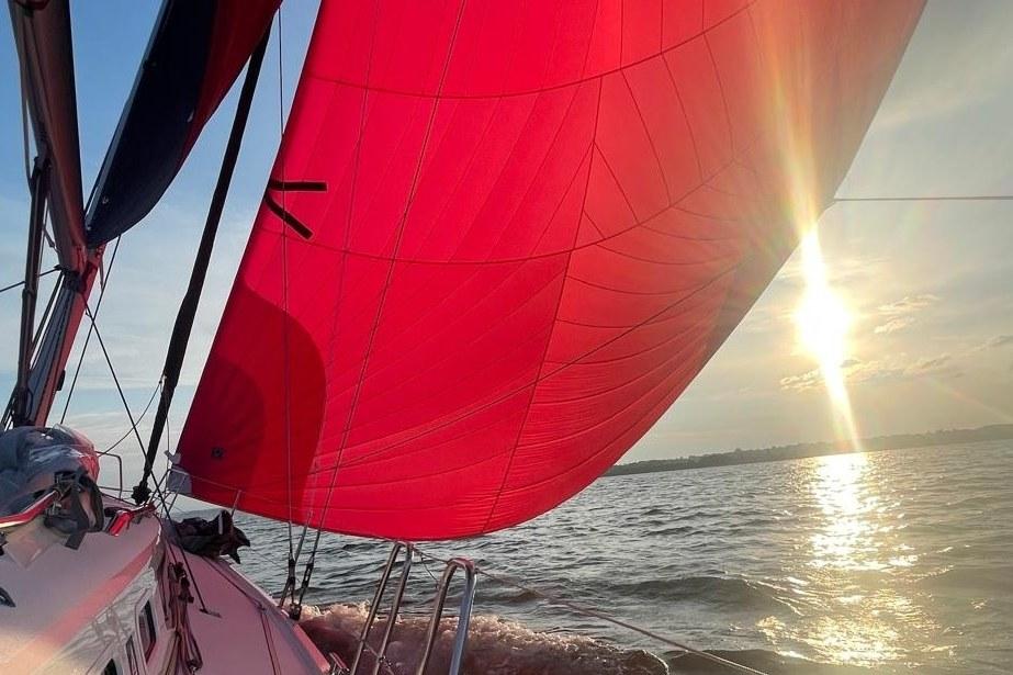 Segelyacht unter rotem Gennaker, tief stehende Sonne über dem Wasser