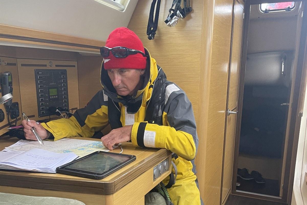 Segler in Ölzeug am Kartentisch einer Yacht, vor sich eine Papierseekarte und ein Tablet