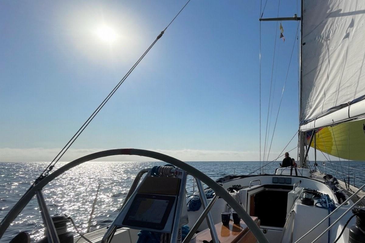 Blick vom Steuerstand einer Segelyacht unter Segeln, Sonne über dem Wasser
